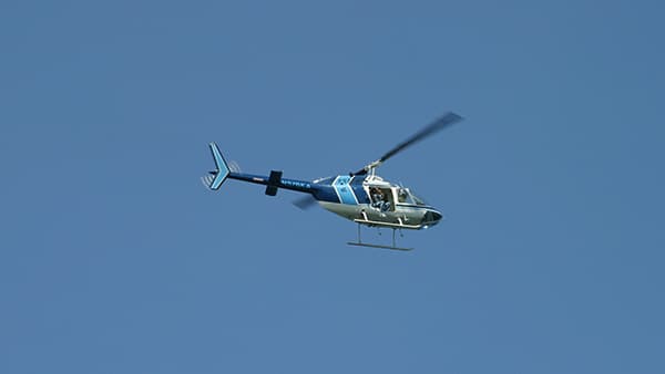 A blue helicopter, with a lighter blue stripe on the back of the cabin and on its tail, is in flight.