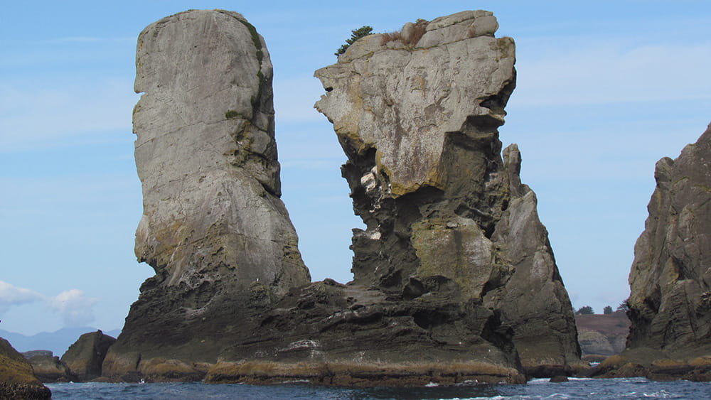 Several tall and jagged sea stacks rise from the ocean, surrounded by blue skies.