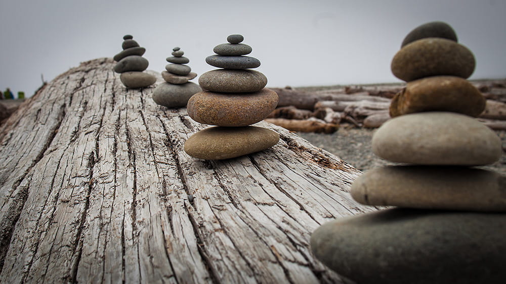 Stones are stacked along a log from big to small, artistically in a line, at the beach.