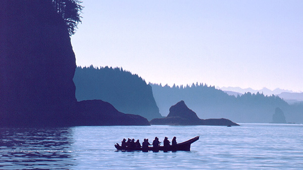 people paddle a tribal canoe near a rocky coast